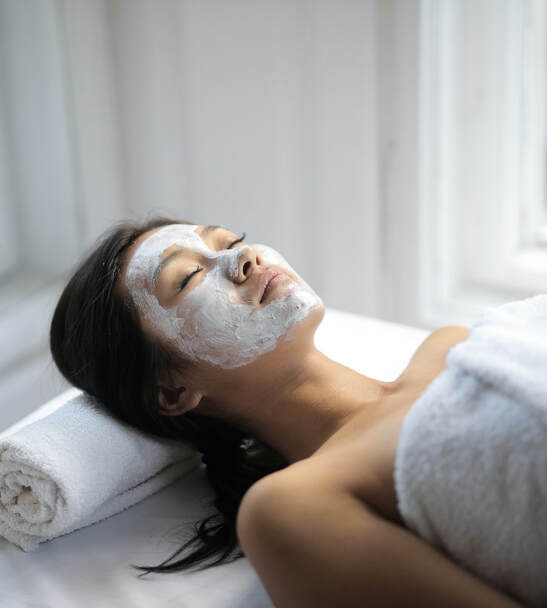 woman serenely lies down, wearing towel and with white cream on her face