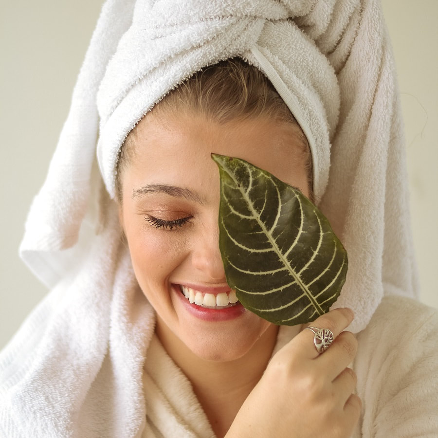 woman in ahir towel and robe laughs while holding a leaf over one eye