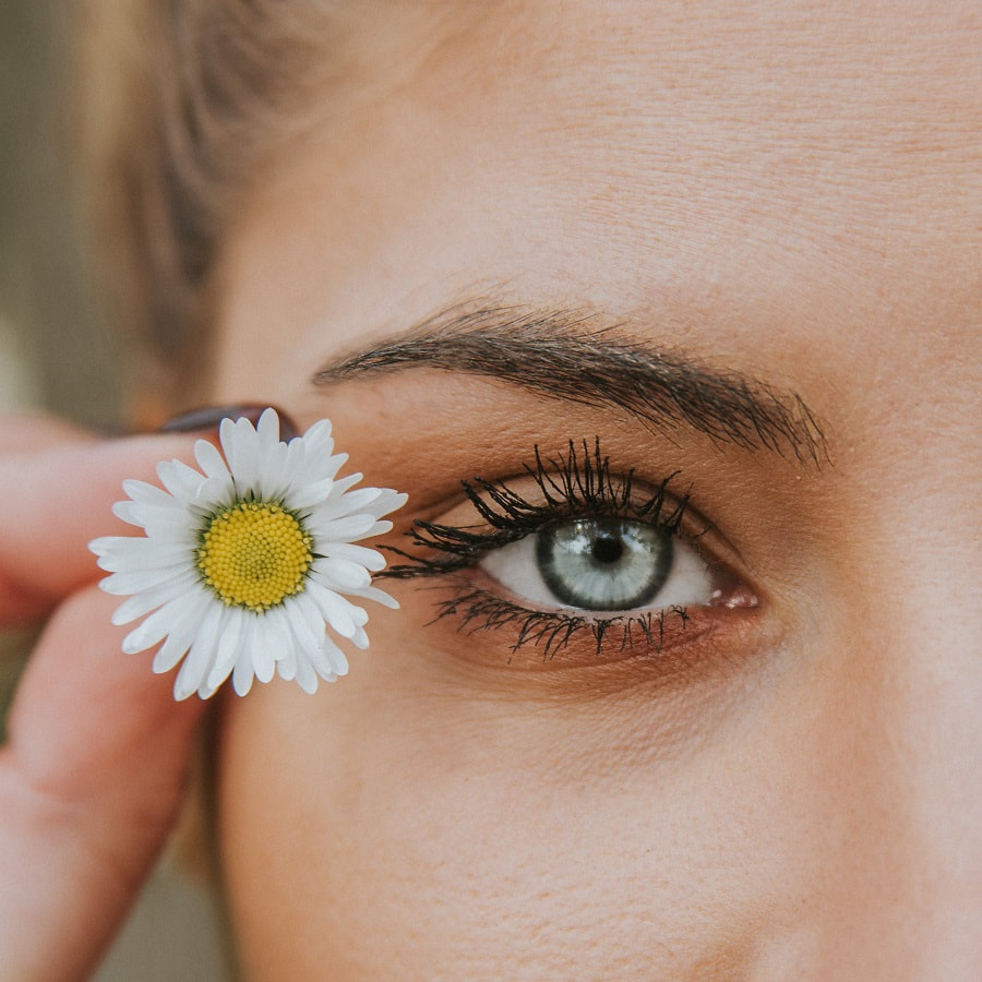 woman with blue eyes holds daisy next to her eye